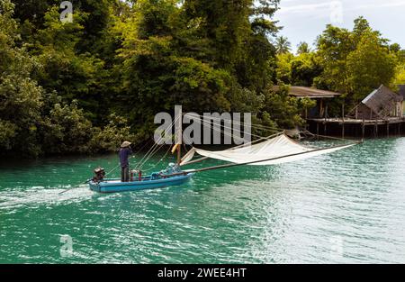 Un pescatore asiatico con un cappello a cono galleggia lungo il fiume su una barca da pesca motorizzata con una rete da pesca. Thailandia, Koh Chang. Foto Stock
