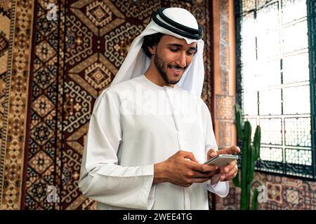 Uomo degli emirati che indossa un abito kandura trascorre del tempo in una casa tradizionale araba a Dubai Foto Stock