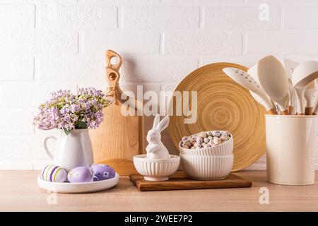 Decorazioni per le vacanze di Pasqua su un piano cucina in legno con utensili da cucina ecologici e uova, coniglietti in ceramica. Concetto di Pasqua Foto Stock