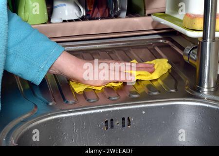 Una donna usa un tovagliolo per rimuovere acqua e sporcizia dalla superficie di un lavello da cucina. Foto Stock