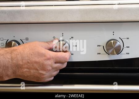 Nella figura, la mano maschile che ruota la maniglia sul pannello del forno. Foto Stock