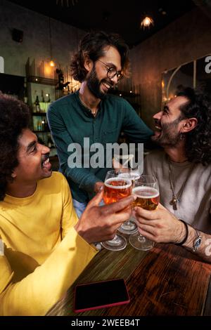 Gruppo di tre amici maschi riuniti in un bar che brinda con birre, festeggiano insieme. Foto Stock