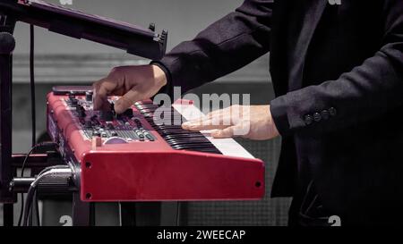 Immagine della mano di un musicista sulle chiavi di un pianoforte a elettrodo rosso Foto Stock