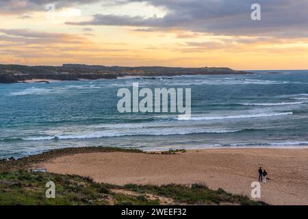 Una giovane coppia guarda il tramonto sulla spiaggia di Zambujera do mar (Portogallo) Foto Stock