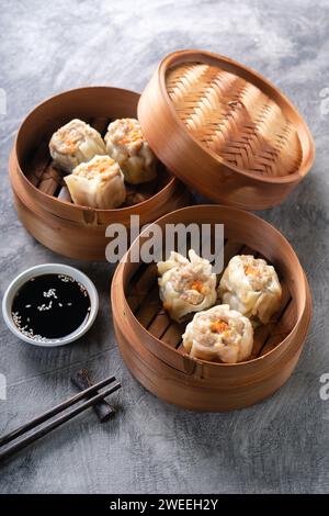 Gnocchi cinesi al vapore o Dim Sum in una vaporiera di bambù su sfondo astratto scuro Foto Stock