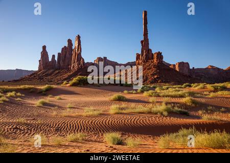 Totem Pole e Yei Bi Chei con dune di sabbia ondulate nel Monument Valley Navajo Tribal Park in Arizona. Foto Stock