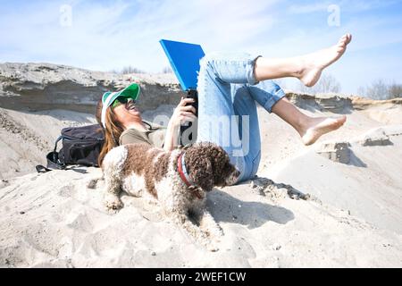 giovane donna che usa un computer portatile nel deserto e si diverte con il suo cane Foto Stock