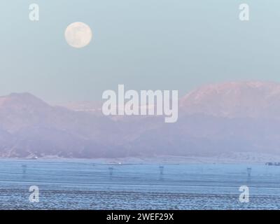 HAMI, CINA - 25 GENNAIO 2024 - Una luna luminosa sorge sui monti Tianshan orientali a Hami, provincia dello Xinjiang, Cina, 25 gennaio 2024. Il primo pieno Foto Stock