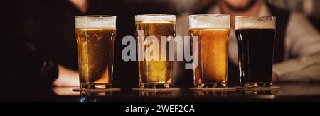 quattro bicchieri con birre diverse al banco del bar in pub sullo sfondo dei baristi Foto Stock