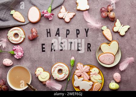 Testo di Pasqua felice tra biscotti pasquali decorati, fiori rosa, tazza di caffè e uova deposte. Sfondo elegante primaverile. Foto Stock