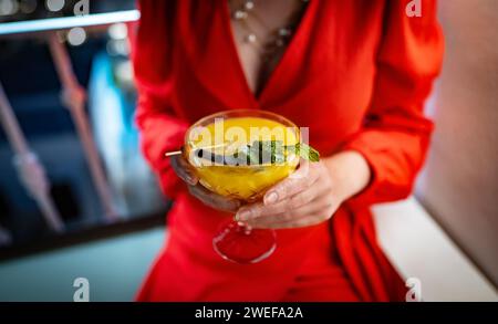 Donna in abito rosso che beve cocktail daiquiri di mango. Foto Stock