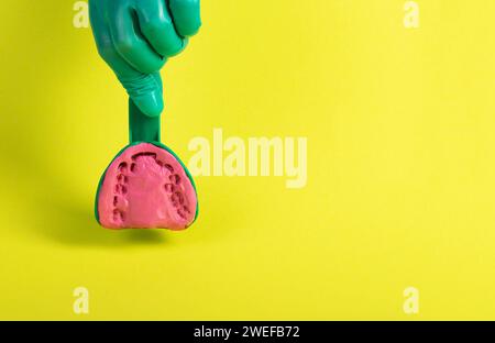 La mano di un medico dentista in un guanto medico verde contiene un cucchiaio dentale con una massa plastica alginata per fare un gesso del paziente s ja Foto Stock