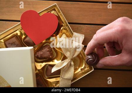 Confezione regalo con fiocco dorato con assortimento di cioccolatini su tavolo in legno e cioccolatini da provare a mano. Vista dall'alto. Foto Stock