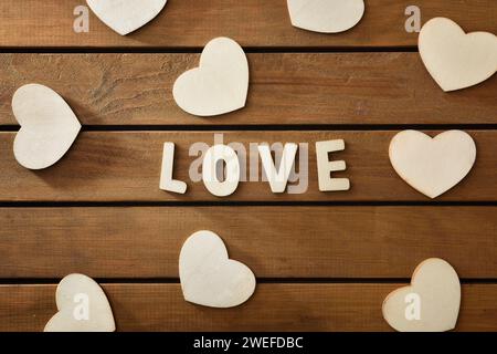 Sfondo con ritagli in legno con lettere che formano l'amore per le parole e cuori sparsi su un tavolo a lastre di legno. Vista dall'alto. Foto Stock