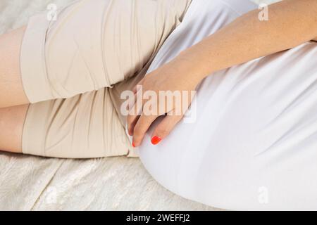 una ragazza incinta giace sul letto e le tiene lo stomaco. Concetto di cistite e infiammazione del tratto urinario e della vescica nelle donne in gravidanza, ormone Foto Stock