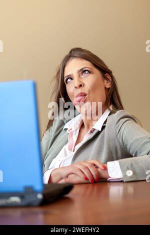 giovane donna d'affari che fa un volto divertente mentre lavora su un notebook Foto Stock