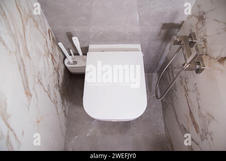 Bagno con moderno WC a parete con piastrelle in gres porcellanato grigio. Doccia igienica e spazzole per WC, primo piano Foto Stock