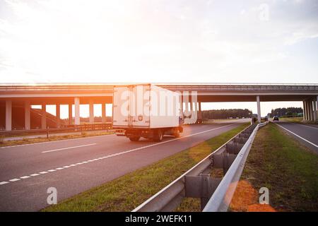 Un furgone commerciale refrigerato a basso tonnellaggio trasporta prodotti deperibili in estate su una strada di campagna sullo sfondo del tramonto. Industria Foto Stock