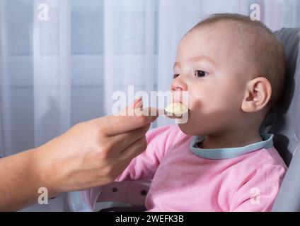 La mano della madre nutre il porridge di zucca del bambino. Ritratto di un bambino di un anno, primo piano. Spazio di copia per il testo Foto Stock