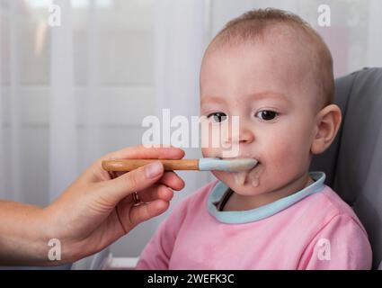 La mano di una madre con un cucchiaio e porridge di grano saraceno nutre un bambino di un anno. Nutrizione dei bambini in tenera età. Alimenti per bambini. Copia Foto Stock