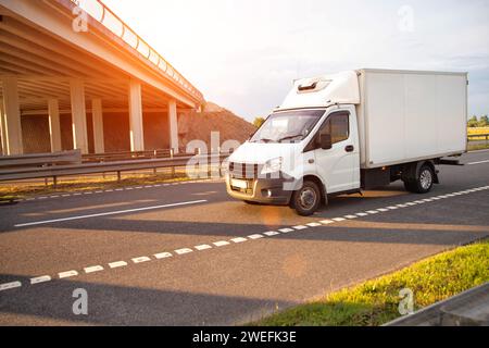 Un furgone commerciale refrigerato a basso tonnellaggio trasporta prodotti deperibili in estate su una strada di campagna sullo sfondo del tramonto. Industria Foto Stock