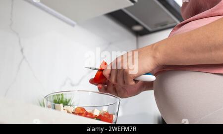 Una ragazza incinta prepara un'insalata di verdure di cetrioli e pomodori. Il concetto di nutrizione delle donne incinte con vitamine e macronutrienti in v Foto Stock