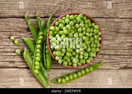 Piselli verdi sbucciati in un recipiente di argilla, piselli verdi biologici dolci in cialde chiuse e aperte e grani sparsi su uno sfondo di legno invecchiato, vista dall'alto. Foto Stock