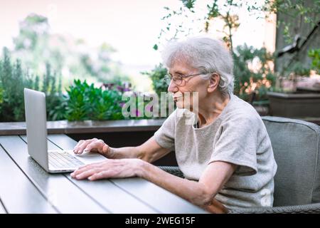 donna anziana che usa un computer portatile sulla terrazza Foto Stock