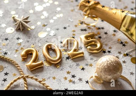 Foto dorata con numeri di Capodanno 2025 circondati da coriandoli e decorazioni. Foto Stock