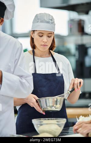 giovane chef con toque e grembiule che prepara l'impasto prima di cuocere e dolciumi Foto Stock