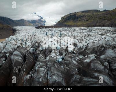 Suggestivo paesaggio islandese di lingua glaciale che sgorga dalla calotta ghiacciata, con una parete glaciale sullo sfondo nella cupa giornata invernale, colpo di drone. Foto Stock