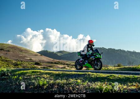 Una moto solitaria che corre lungo una cresta di montagna con paesaggi spettacolari e nuvole sullo sfondo Foto Stock