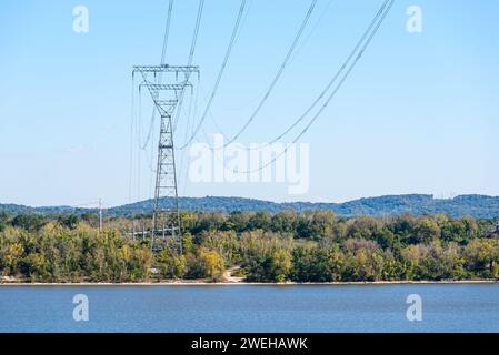 Alto pilone elettrico che supporta linee ad alta tensione sulla riva di un fiume in una soleggiata giornata autunnale Foto Stock