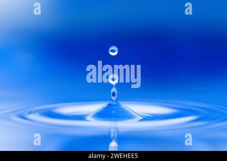 le goccioline d'acqua saltano dalla superficie blu dell'acqua Foto Stock