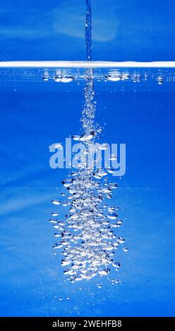 un sottile getto d'acqua penetra nella superficie dell'acqua e produce molte bolle d'aria nell'acqua blu di un acquario Foto Stock