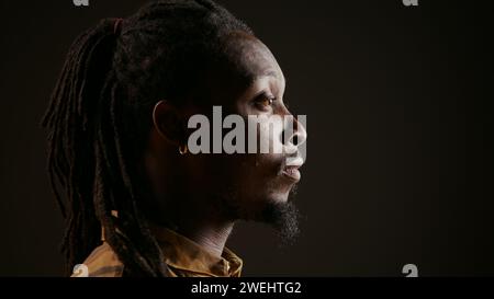 Elegante modello maschile che si comporta sorpreso e stupito dalla vista, vedendo qualcosa e rimanendo scioccato. Un ragazzo afro-americano che ammira una cosa e dice wow in studio con sfondo nero. Foto Stock