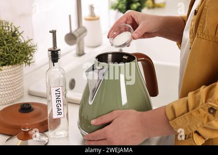 Donna che aggiunge bicarbonato di sodio nel bollitore elettrico in cucina, primo piano Foto Stock