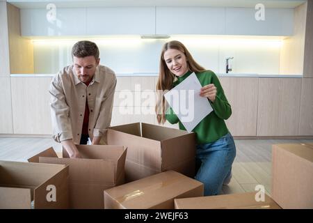 Moglie e marito che disimballano le scatole dopo essersi trasferiti in un nuovo appartamento a controllare la lista. Trasferimento. Foto Stock