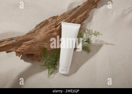 Scena di mockup per cosmetici con flacone di plastica bianco senza marchio su sfondo sabbioso con ramoscello asciutto e foglie verdi. Concetto naturale Foto Stock