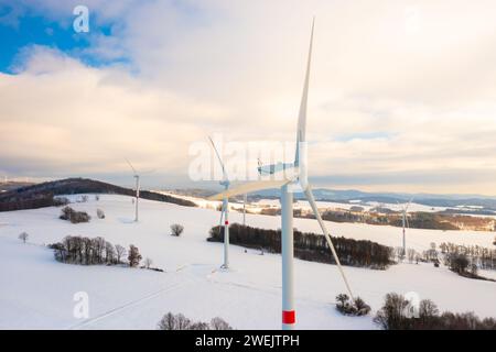 Vista aerea delle turbine eoliche o dei mulini a vento sul campo invernale contro il cielo nuvoloso durante il tramonto Foto Stock