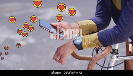 Icone a forma di cuore multiple che fluttuano contro la sezione centrale di una donna con una bicicletta che utilizza lo smartphone Foto Stock