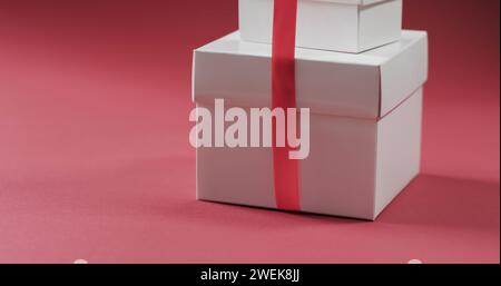 Scatole regalo bianche con un nastro rosso su sfondo rosa Foto Stock