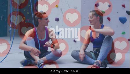 Icone multiple del cuore che fluttuano contro due donne caucasiche che battono in palestra Foto Stock