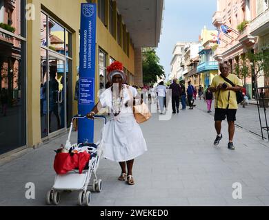 Una donna cubana vestita in modo tradizionale che cammina su una strada principale nella vecchia Avana, Cuba. Foto Stock