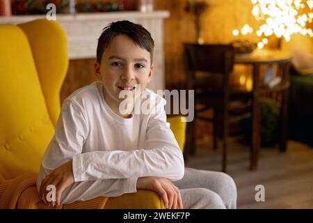 Bambino adolescente, ragazzo, seduto in una comoda poltrona a casa, sorridendo davanti alla macchina fotografica Foto Stock