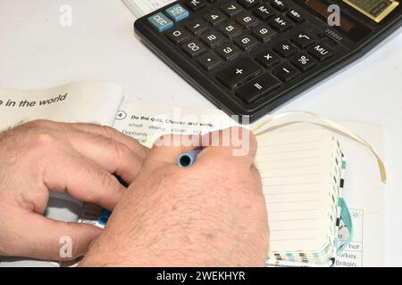 L'immagine mostra un uomo che scrive le mani in un notebook. Un uomo siede a un tavolo con una calcolatrice e dei documenti. Foto Stock