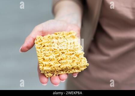 Mano che regge spaghetti gialli essiccati su sfondo bianco. Foto Stock