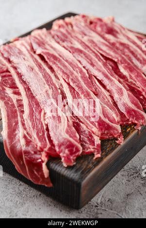 Vista ravvicinata delle strisce di pancetta di manzo crudo fresco su un tagliere di legno Foto Stock