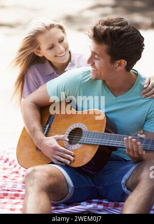 Coppia felice, picnic e chitarra per romanticismo, amore o musica all'aperto, divertimento o relax insieme nella natura. Uomo e donna sorridono con Foto Stock