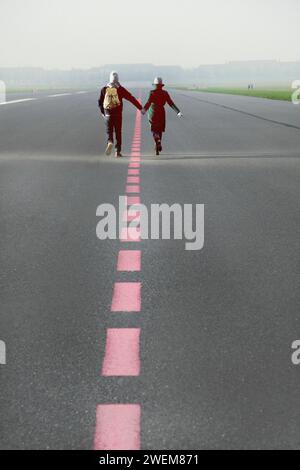 Matura in esecuzione lungo la pista di aeroporto Holding Hands, vista posteriore Foto Stock